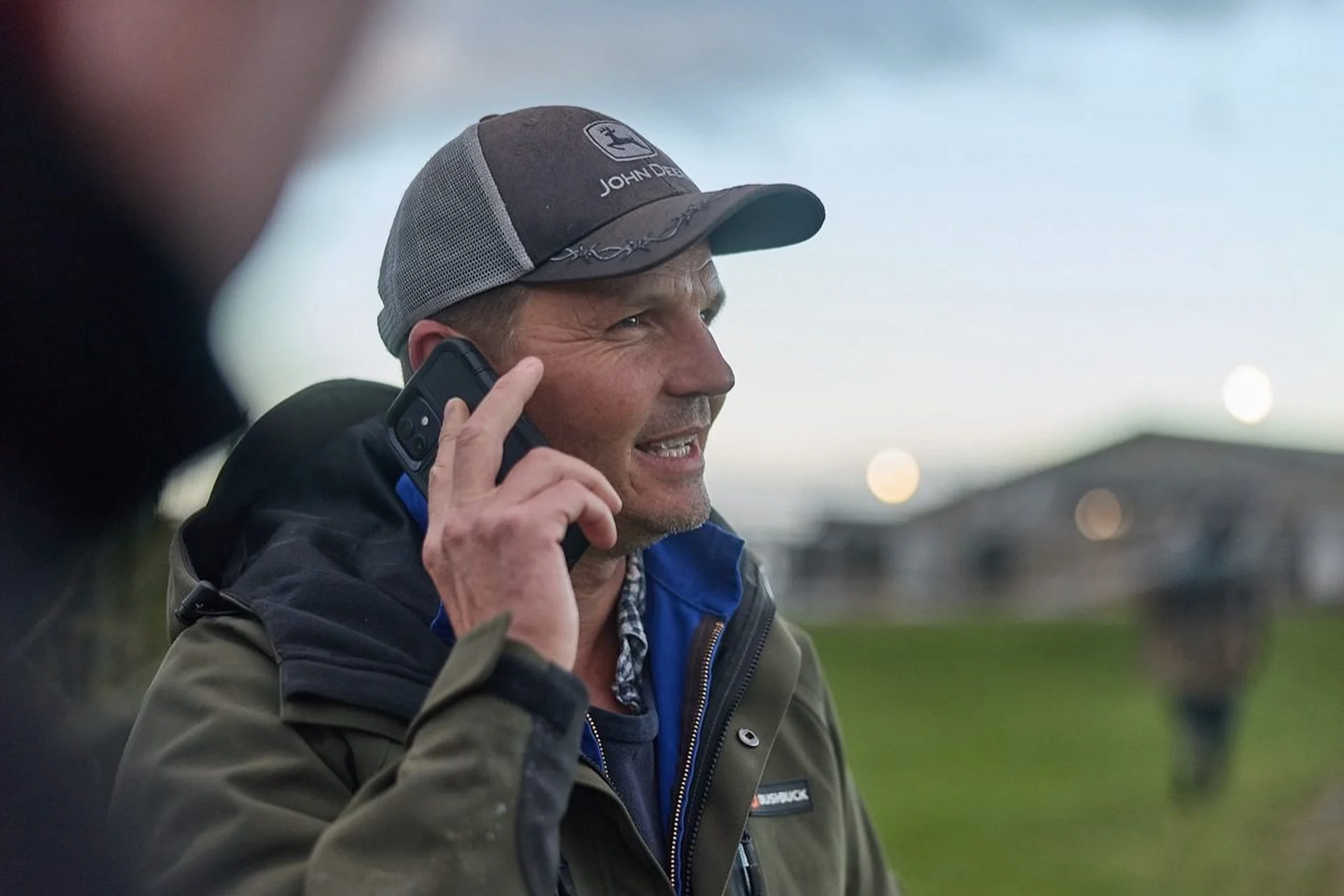 Contact Farmlands: Man in a cap smiling while talking on a phone outdoors.