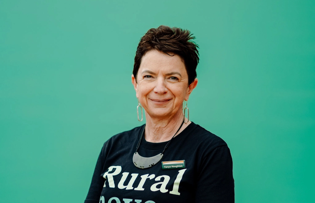 Tanya Houghton in a black shirt with "Rural never rests." stands smiling against a green background.