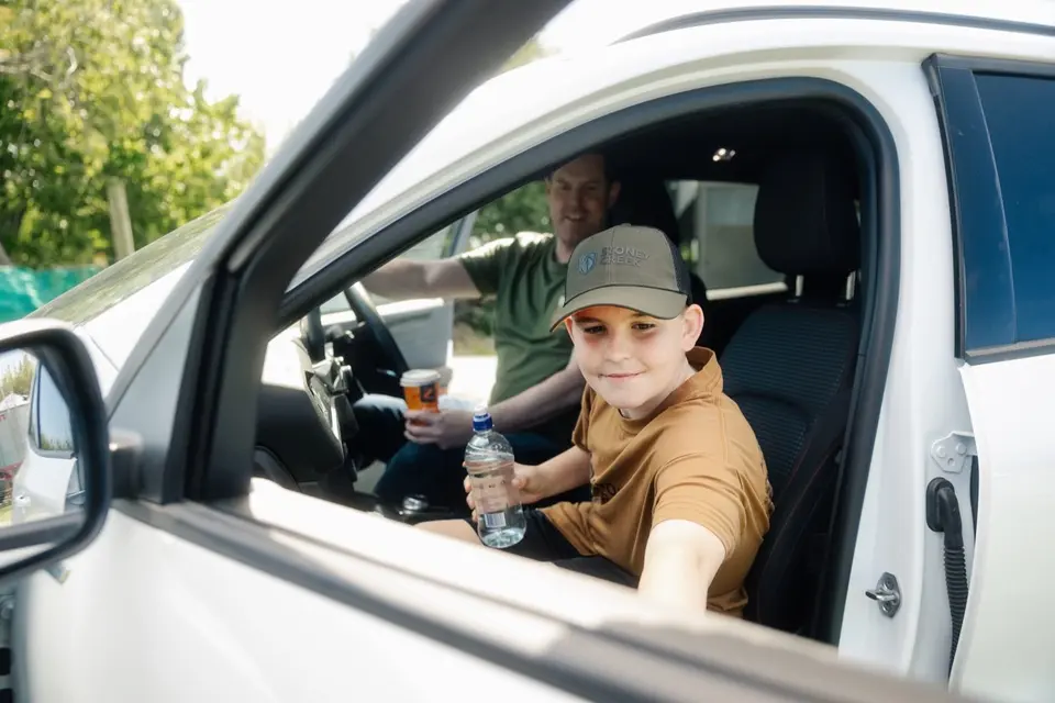 Farmlands Card: A boy in a cap sits in a car's passenger seat holding a water bottle, with a man in the driver's seat.