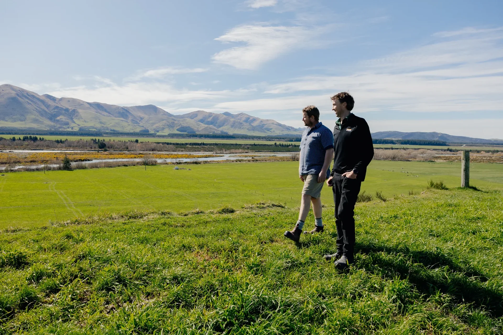 Two people walking on a grassy hill with mountain views