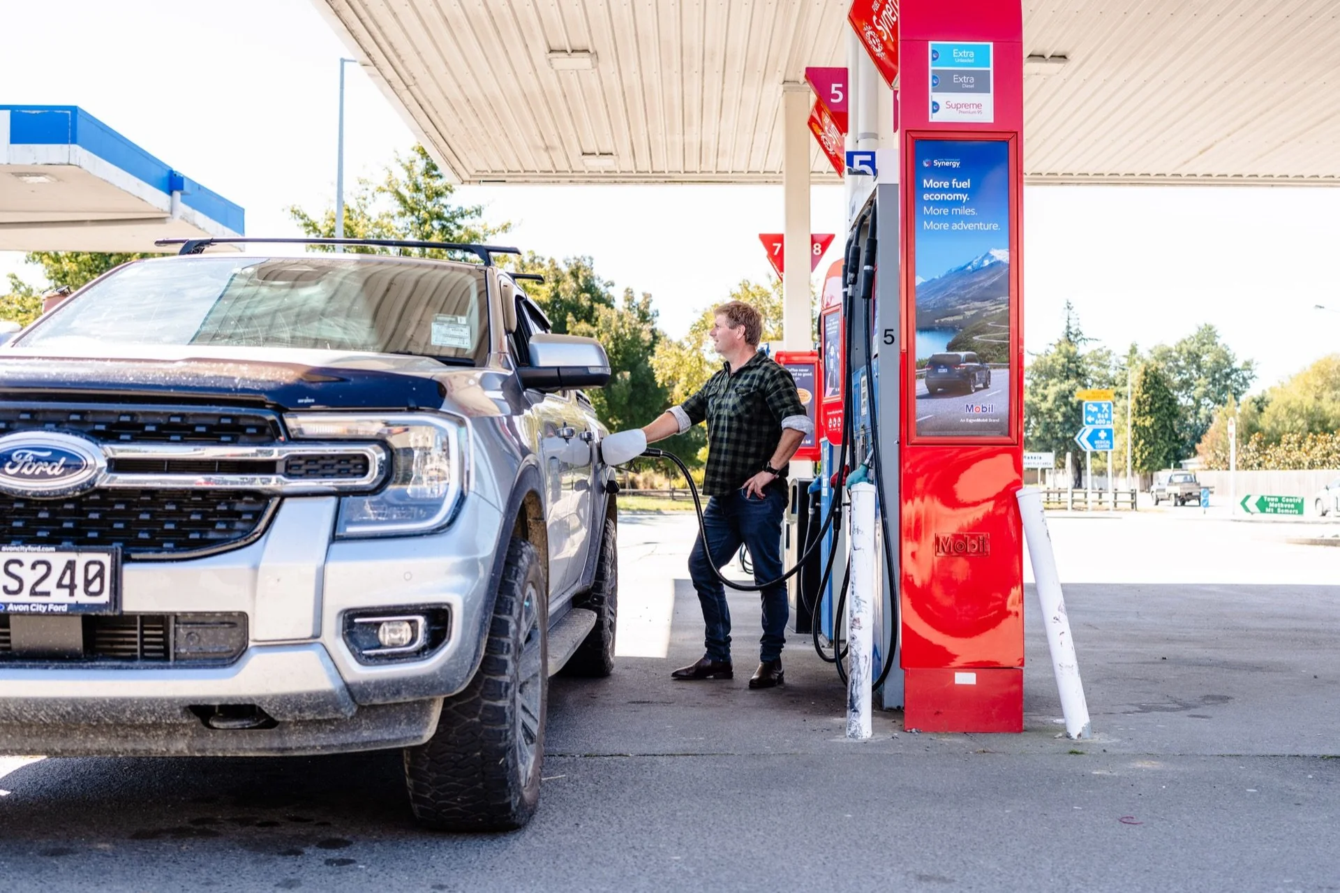 Farmlands fuel: Person refueling a Ford truck at a gas station, with a red and white pump and a sunny outdoor setting.
