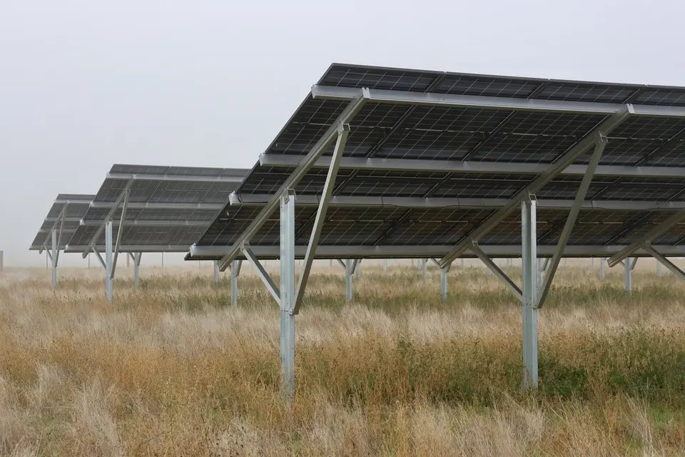 Knowledge and advice: Rows of solar panels on metal frames in a grassy field under a cloudy sky.