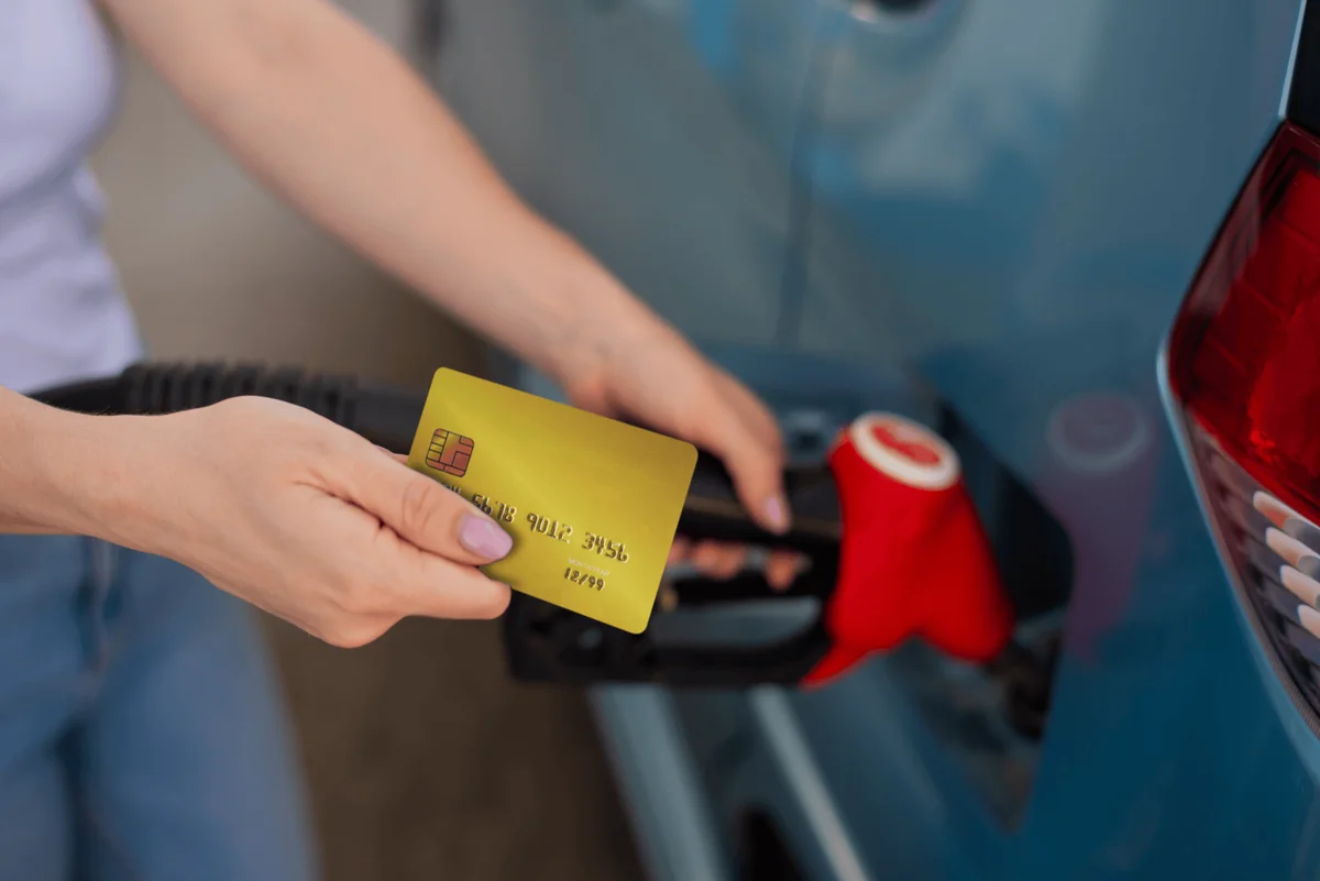 Farmlands fuel: Person holding a yellow credit card, fueling a car with a red gas nozzle at a gas station.