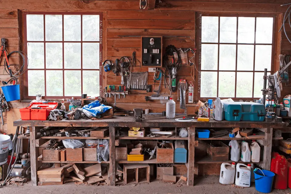 Preventing rural crime in NZ: A cluttered workshop with tools hanging on a wooden wall, a workbench filled with supplies