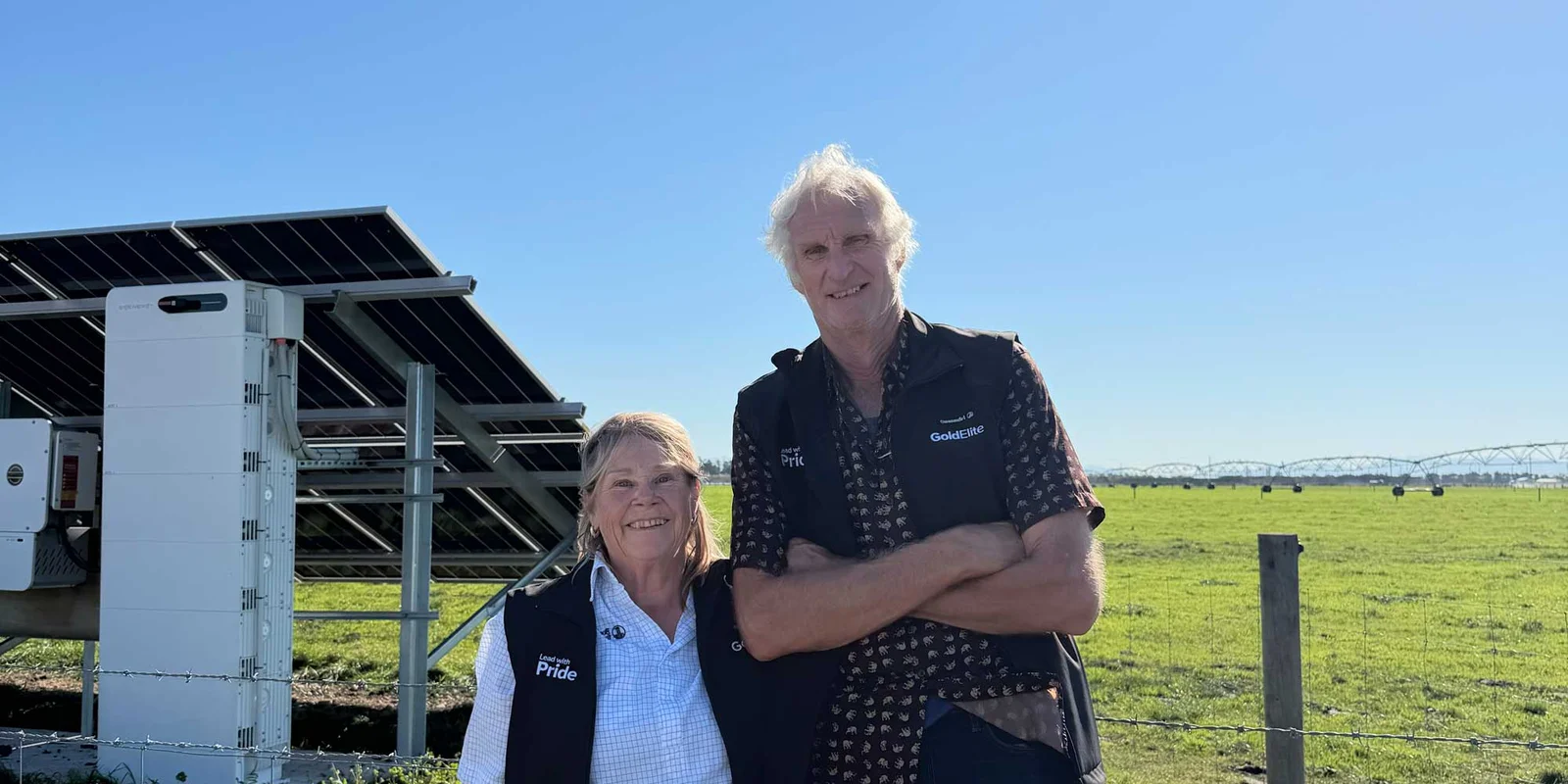 Chris and Pauline Prattley stand smiling in front of solar panels in a sunny field.